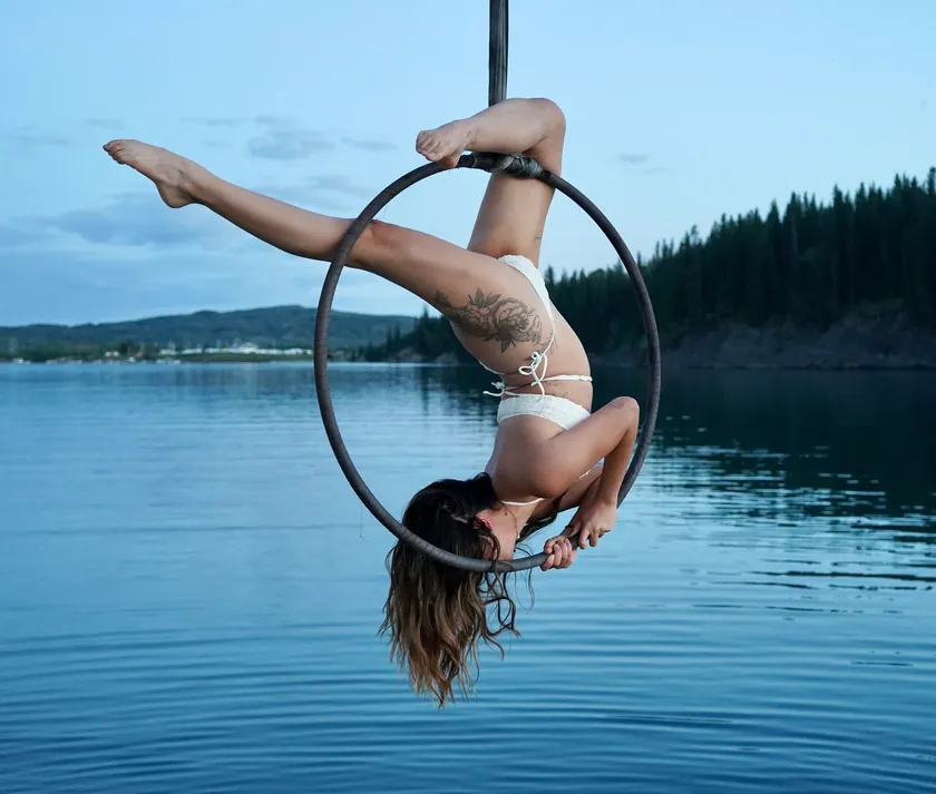 An aerialist inverted in an aerial hoop suspended over the lake