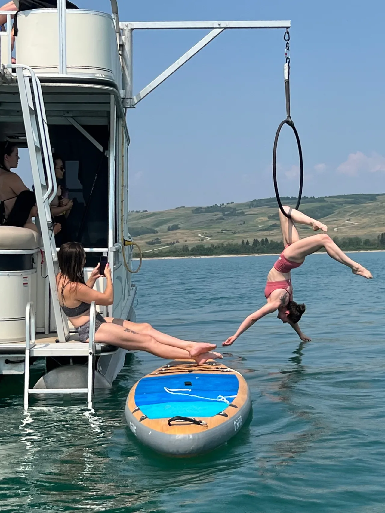 An aerial hoop rigged off the side of the boat, reached from a paddleboard