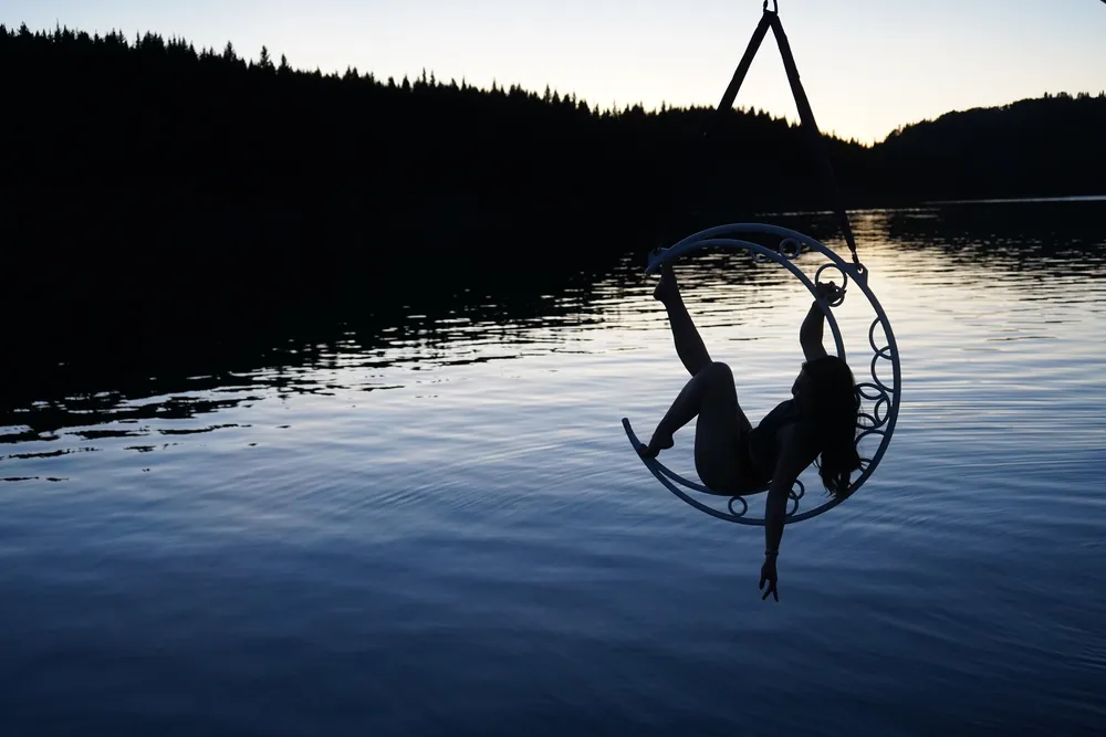An aerialist silhouetted in the hoop against the lake at dusk