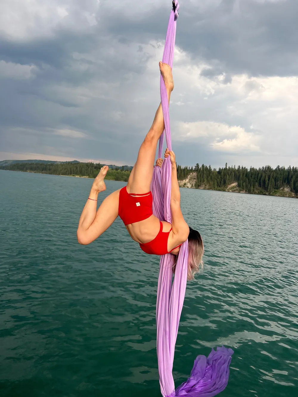An aerialist in red on pink silks suspended above the lake