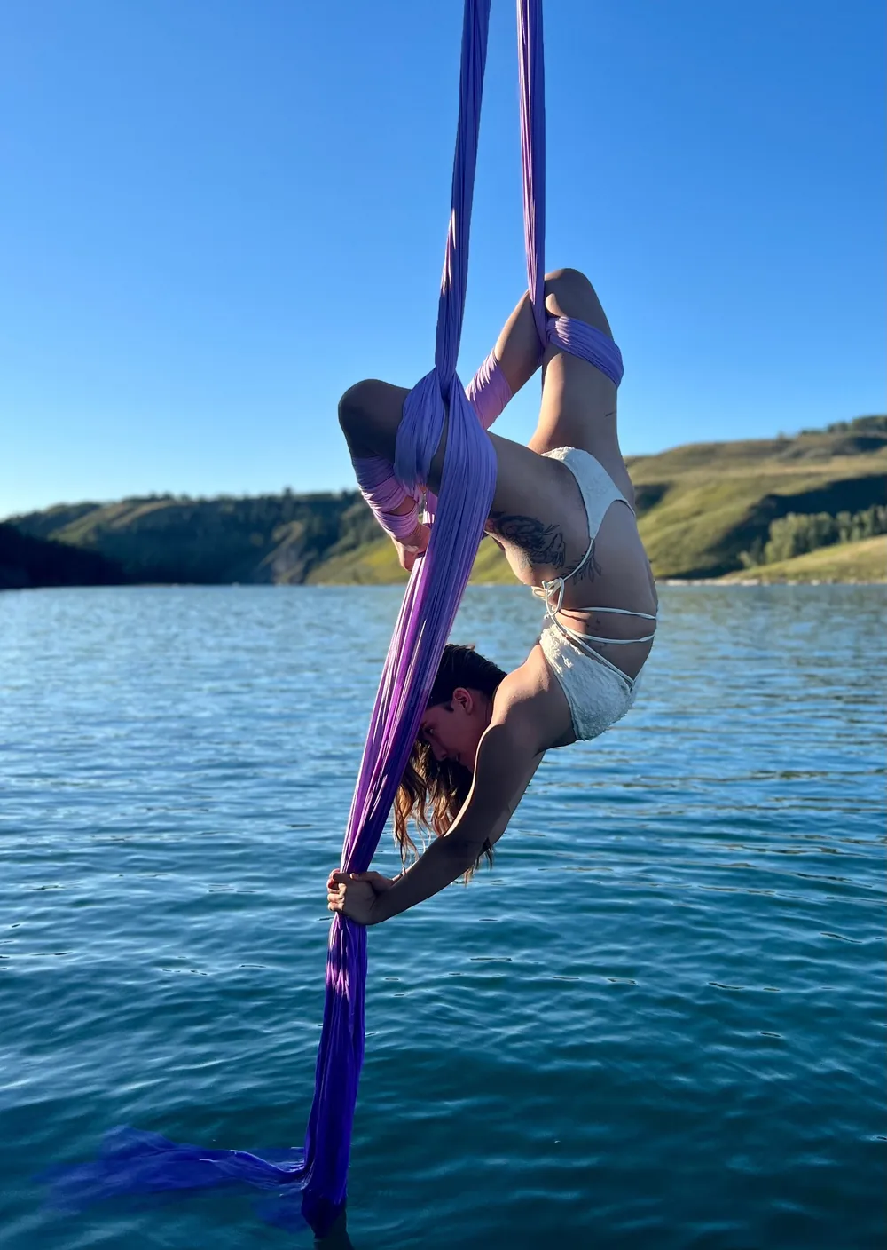 An aerialist wrapped in purple aerial silks over the water