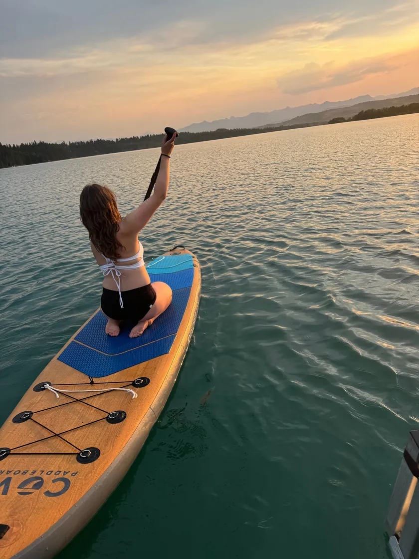 A guest paddleboarding beside the boat at sunset