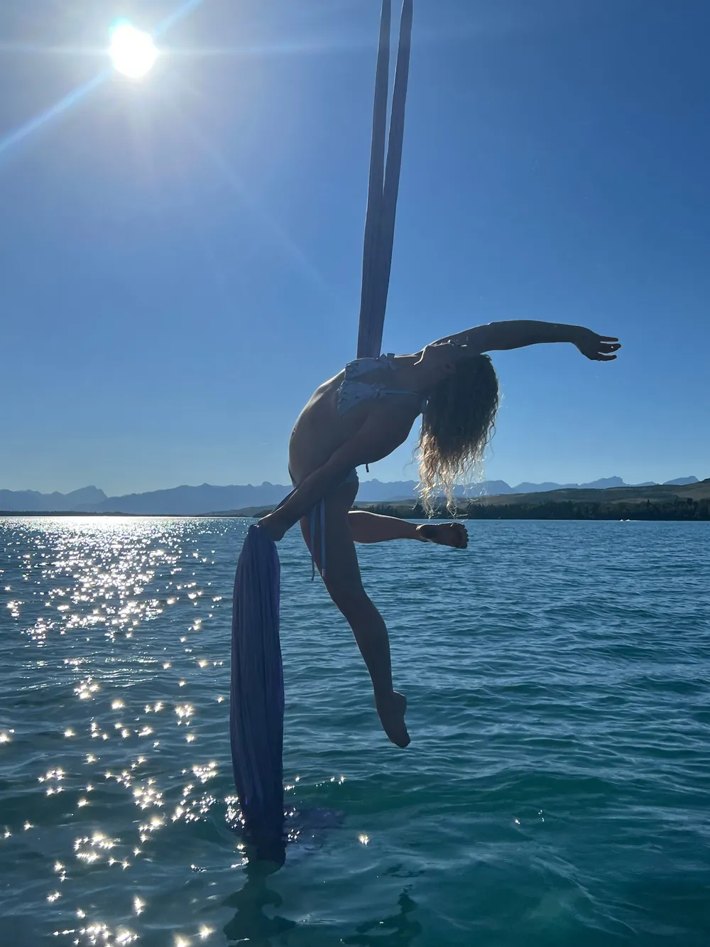 A dancer in a backbend on the deck pole with the sun flaring behind