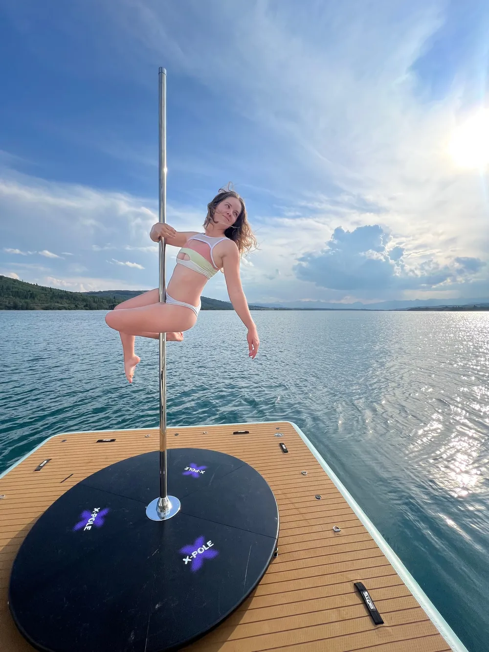 A dancer on the floating-dock pole under a wide cloudy sky